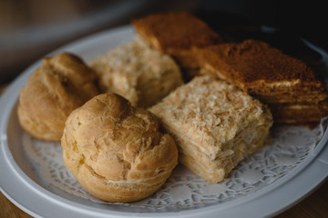 Different types of European pastries (napoleon, walnaut and eclair cakes) on white plate on blurred...