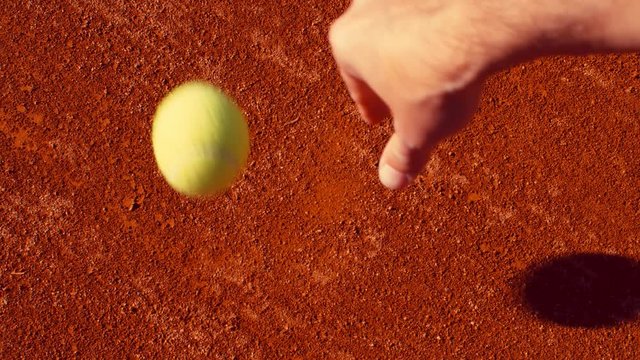 Tennis player bouncing tennis ball on a red tennis court before serving, 4k, slow motion 75fps