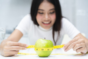 eating healthy and dieting concept. Girl use measure tape measuring green apple on the table.