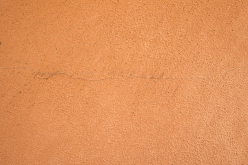 Terracotta, burnt sienna colored wall of house or building with scratch coat plaster work painted in orange peach color with rough texture, already some years old with cracks, filthy and dirty