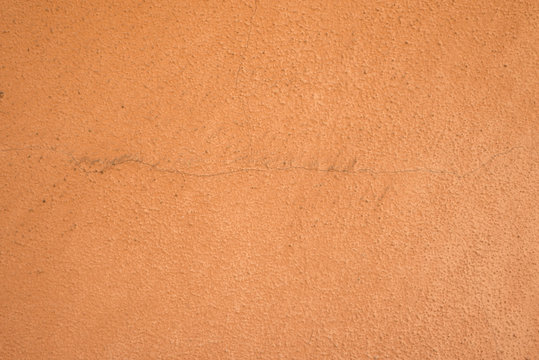 Terracotta, burnt sienna colored wall of house or building with scratch coat plaster work painted in orange peach color with rough texture, already some years old with cracks, filthy and dirty