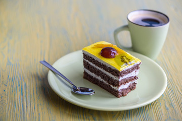 Chocolate puff cake with cherry on top and a cup of coffee photographed close-up on a wooden background.
