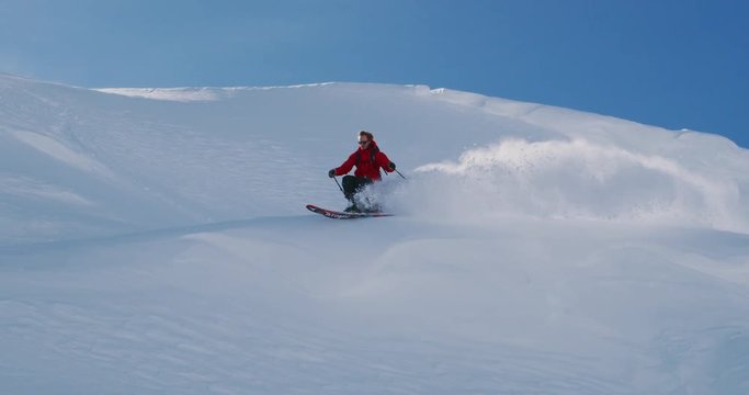 Skier doing powder turn and jumping off snow cliff, amazing bluebird backcountry day, ski adventure, slow motion skiing