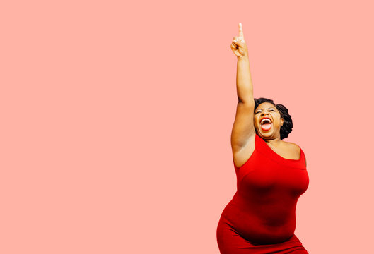 Horizontal portrait of a very happy and excited woman celebrating success with arm up, mouth open and finger pointing up	