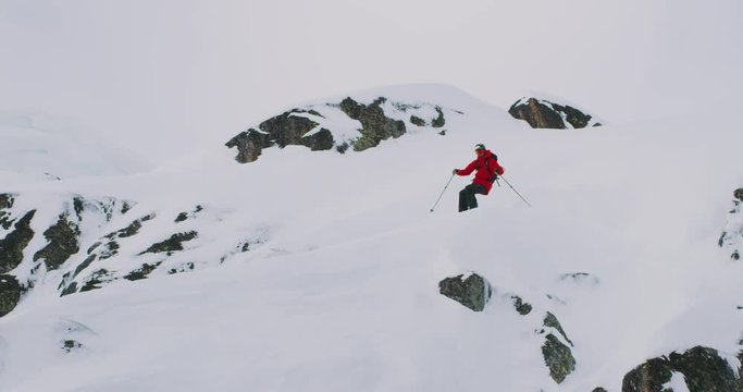 Skier doing powder turn and jumping off of ice cliff, extreme backcountry skiing, slow motion