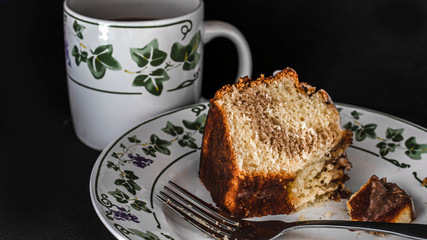 A piece of cake on a plate with a cup of hot chocolate.
