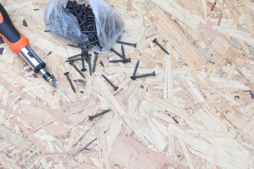 Screwdriver with black screws on the background of the OSB panel. Concept on the topic of building and repair.