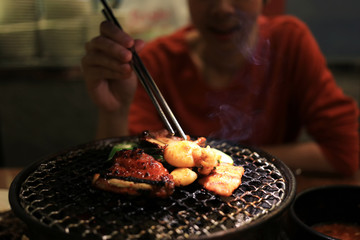 Woman enjoying grilling barbecue on mesh grill of charcoal fire. Korean or japanese traditional roast food style barbecue.