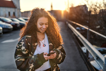 Fototapeta premium Beautiful smiling mixed race teenage girl in military jacket standing outdoors and writing message.