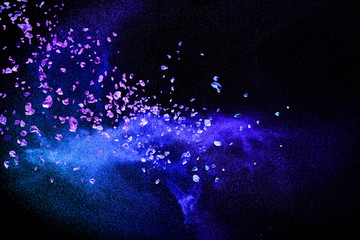 Split debris of purple stone exploding with blue dry river sand against black background.