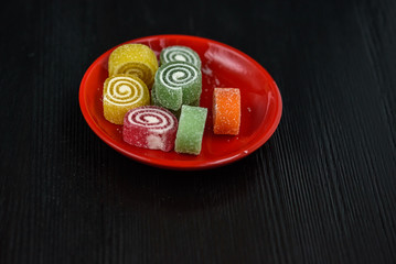 Multicolored marmalade on a red plate on a black wooden background