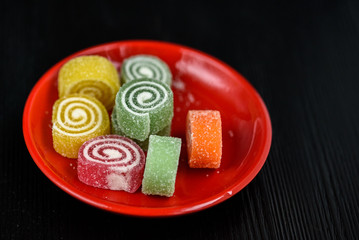 Multicolored marmalade on a red plate on a black wooden background