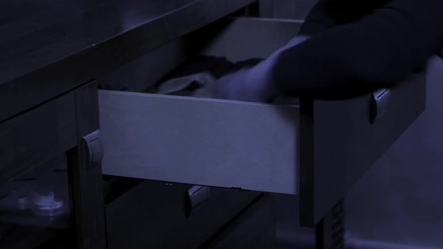 burglar rummages through a closet, discarding things and finding a lot of money. Close-up.