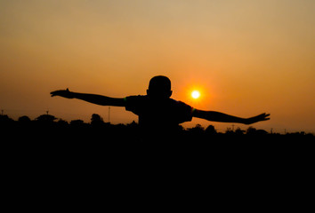 Silhouette of Asian teen boy jumping at the field with sunset background in evening.