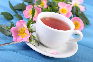 Fototapeta na wymiar Cup of hot tea and wild rose flower on boards