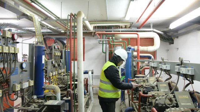 Engineer looking at the high pressure air compressor and writing.	