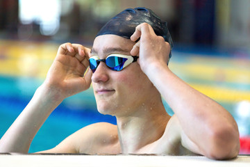 A teenage athlete improves swimming goggles in an indoor pool. Close up, selective focus.