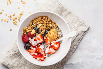 Granola with milk, chia, berries and peanut butter in a white bowl, top view.