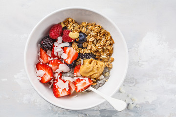 Granola with milk, chia, berries and peanut butter in a white bowl, top view.
