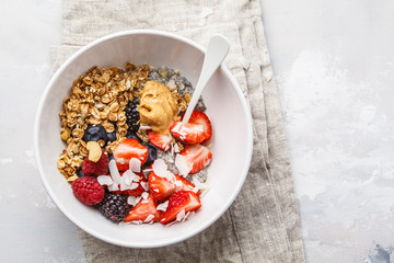 Granola with milk, chia, berries and peanut butter in a white bowl, top view.