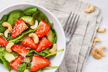 Summer strawberry avocado salad with cashews in a white bowl, top view.