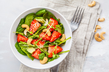 Summer strawberry avocado salad with cashews in a white bowl, top view.