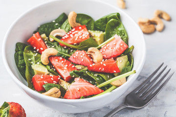 Summer strawberry avocado salad with cashews in a white bowl.