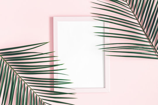 Summer composition. Tropical palm leaves, pink photo frame on pink background. Summer, nature concept. Flat lay, top view, copy space