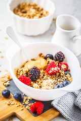 Breakfast food background. Granola with hemp seeds, maca powder, peanut butter and berries on white table.