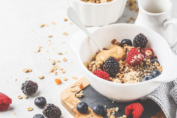 Breakfast food background. Granola with hemp seeds, maca powder, peanut butter and berries on white table.