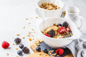 Breakfast food background. Granola with hemp seeds, maca powder, peanut butter and berries on white table.