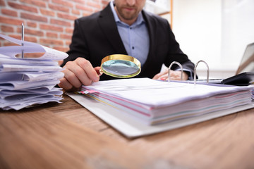 Businessman Examining Invoice Through Magnifying Glass