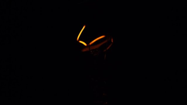 Tungsten light bulb lamp blinking over black background, macro shot