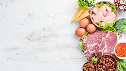Food high in protein on table. Meat, chicken fillet, broccoli, beans, cheese, eggs, wheat. On a white wooden background.