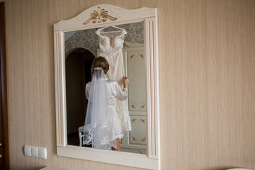 bride in bathrobe holding wedding dress in hands