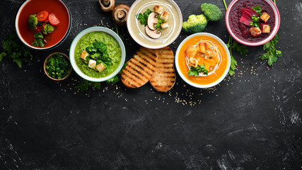 Assortment of colored vegetable cream soups. Dietary food. On a black stone background. Top view. Free copy space.