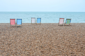 Three pairs of beach chairs with red, blue, white and yellow stripes on beach, towards sea water