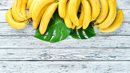 Banana with green leaves on a white wooden table. Tropical Fruits. Top view. Free copy space.