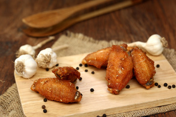 Beautiful plate fried chicken wings on wooden tray with garlic and pepper, selective focus and free copy space. Clean food good taste concept.