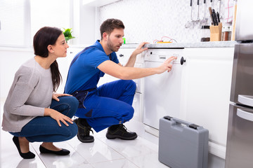 Serviceman Pressing Button Of Dishwasher In Kitchen