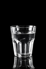 Glass of water on black reflective background.