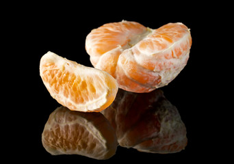 Tangerines or mandarins slices on black reflective background.