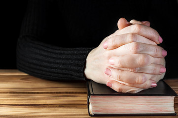Woman praying over table with Holy Bible. Close up. Space for text.