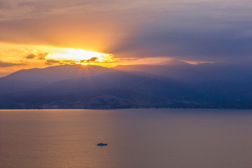 dramatic colorful landscape in sunset time with lake foreground and mountain background with yellow and orange sun rays from above ridge