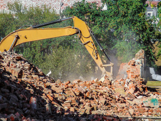 Dismantling a brick building with a bucket excavator. Ruins and remains of walls.