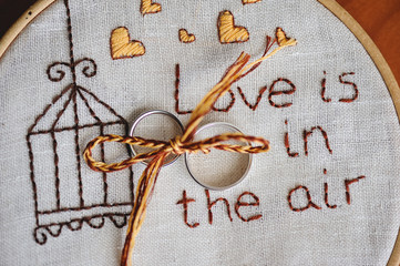 anillos de oro de boda sobre bastidor de bordas con las palabras love is in the air bordadas
