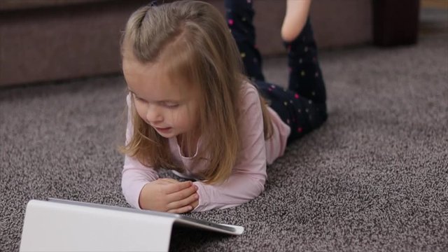 Happy little child, adorable blonde toddler girl enjoying using tablet pc