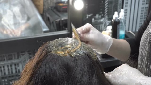 Barber puts paint on the hair of a girl in a beauty salon. Hair care. Close up. The view from the top rear. 4k. 25 fps.