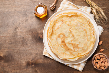 Crepes, thin pancakes with honey and nuts on a white plate . Wooden background . - obrazy, fototapety, plakaty
