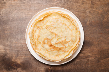 Crepes, thin pancakes with honey and nuts on a white plate . Wooden background .